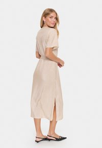 Rochie midi ribbed bej cu mâneci scurte, talie marcată cu brâu și fante pe lateral. Pur tată cu balerini negri cu vârful ascuțit și bijuterii argintii minimale.