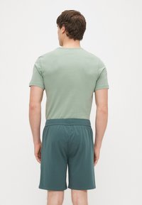 Roupa masculina com uma camisa de manga curta verde-claro e calções azul-petróleo. A camisa tem decote redondo e os calções possuem cintura elástica.