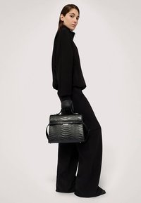 Svart handväska med krokodilmönstrad präglad yta, strukturerad design och handtag upptill, matchad med svart oversize-plagg och handskar.