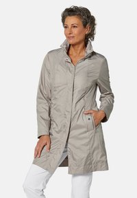 Hellgraue wasserdichte Jacke mit hohem Kragen, Frontreißverschluss, Druckknöpfen und zwei seitlichen Taschen. Glatte Textur mit taillierter Passform.