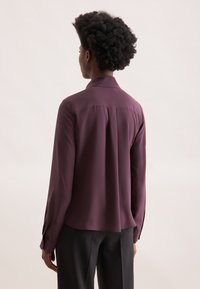 Langärmliges Shirt in tiefem Pflaumenrot, glattes Gewebe mit einem Kragen, Rückenpasse, und Knopfmanschetten; figurbetonte Silhouette, abgerundeter Saum.