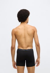 Sorte boksershorts med en elastik i taljen, der har "TOMMY HILFIGER"-logoet i hvidt og rødt. Fremstillet af et glat, elastisk stof.