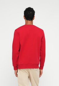 Sweatshirt rouge en mélange de coton, avec un col rond, des manches longues et des poignets côtelés. Design uni sans motifs ni accents visibles.