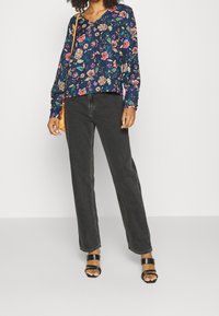 Blusa navy a maniche lunghe con motivi floreali multicolori, abbinata a jeans neri a gamba dritta e sandali neri con tacco.