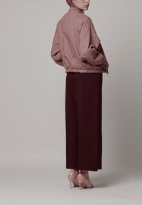 Chaqueta bomber rosa texturizada con cuello alto, combinada con pantalones marrón oscuro de talle alto y tacones nude.