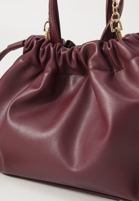 Sac à main en cuir bordeaux avec un design plissé, texture lisse et accents en métal doré. Dispose de poignées courtes et d'une forme structurée.