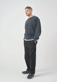Dark gray quarter-zip sweatshirt with a relaxed fit, layered over a white shirt. Paired with black trousers and gray sneakers.