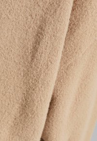 Tissu en laine beige avec une surface douce et texturée et des fibres visibles, présentant des plis naturels et un drapé.