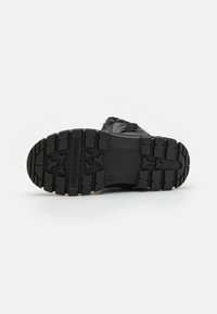 Suola di sneaker nera con scanalature profonde, con la scritta "TOMMY HILFIGER" impressa. Superficie texturizzata con un mix di materiali in gomma e schiuma.