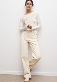 Haut à manches longues crème avec décolleté drapé et pantalon large beige clair. Texture douce et lisse avec des coutures subtiles et une coupe décontractée.