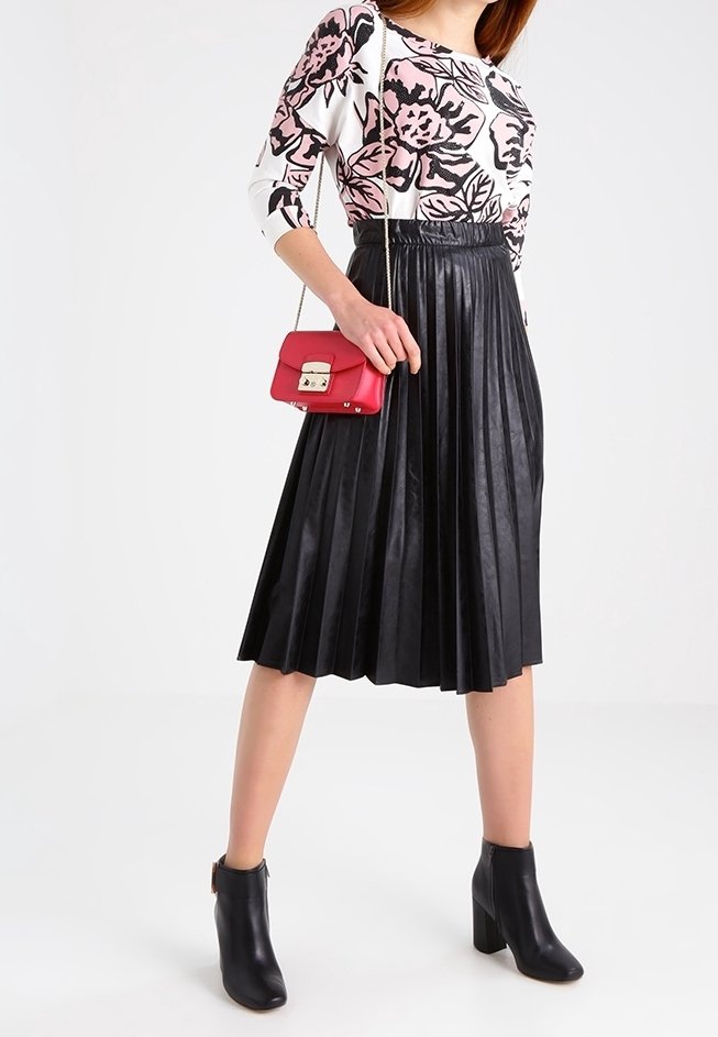 Schwarzer plissierter Midi-Rock kombiniert mit einem weißen Oberteil mit pinken Blumenmustern. Eine kleine rote Handtasche und schwarze Stiefeletten runden das Outfit ab.