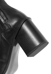 Botín negro de cuero hasta el tobillo con un tacón grueso negro. Presenta costuras mínimas y una textura suave, destacando su diseño elegante.