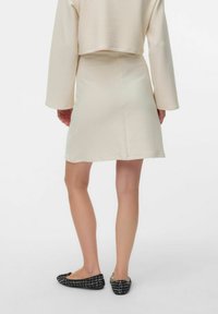 Crème-kleurige, geribbelde, geknipte top met lange mouwen en een bijpassende A-lijn rok. Heeft zwarte en witte gestructureerde slippers.