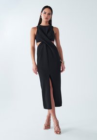 Must must midi-kleit, millel on lõhestatud küljed, vöö juures drapeeritud keerutusdetail ja reie kõrgune lõhik. Modell kannab kuldseid rihmikandades kontsakingi.