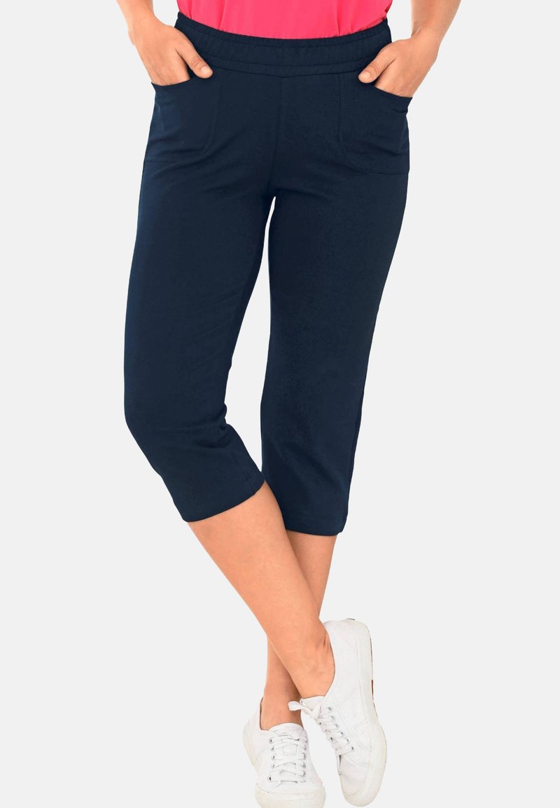 Marineblauwe capri broek met een elastische tailleband en twee voorzakken, met een gladde textuur en een aansluitend ontwerp. Gecombineerd met witte sneakers.
