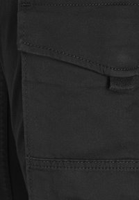 Black cargo pants made of textured fabric featuring a flap pocket with visible stitching detail and a loop for accessories.