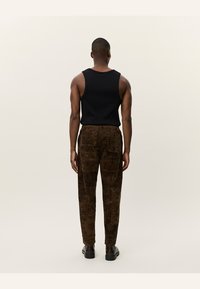 Un maiou negru fără mâneci și pantaloni maro cu pattern. Pantalonii au texturi detaliate și patru buzunare, cu pantofi întunecați.