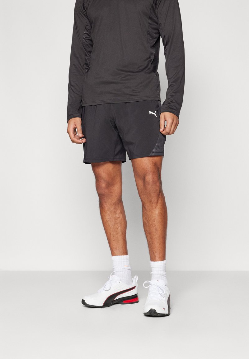 Svart langermet treningsskjorte, svarte shorts med sidelapp, hvite sneakers med røde detaljer, og hvite ankelsokker.