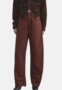 Pantalones de pierna ancha en un color óxido intenso, confeccionados en una tela texturizada; cuentan con trabillas para cinturón y bolsillos, con un ajuste suelto y relajado.