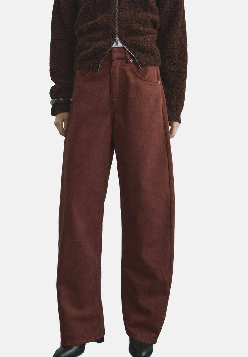 Pantalones de pierna ancha en un color óxido intenso, confeccionados en una tela texturizada; cuentan con trabillas para cinturón y bolsillos, con un ajuste suelto y relajado.