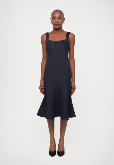 Donker denim jurk met een aansluitend lijfje, vierkante halslijn en uitlopende zoom. De jurk heeft brede schouderbanden en subtiele verticale stiksels.
