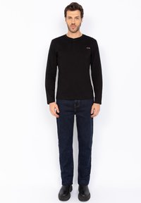 Camicia henley a maniche lunghe nera con scollatura abbottonata e dettaglio della tasca, abbinata a jeans blu scuro e calzature nere.