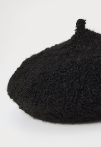 Schwarze Woll-Beret mit einer strukturierten, flauschigen Oberfläche; runde Form und eine kleine Schlaufe oben zur Anpassung oder Dekoration.