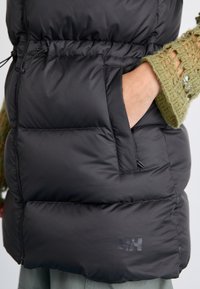 Melnas pūkainas vesta ar quilted dizainu, ar sānu kabatu un elastīgu jostu. Pievienota tekstūrēta zaļa adīta piedurkne.