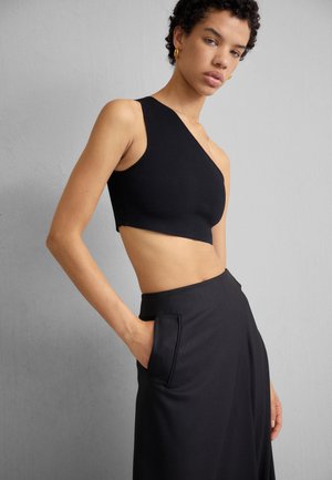 Czarny top crop na jedno ramię z gładkiego materiału, zestawiony z czarną spódnicą o wysokim stanie z bocznymi kieszeniami i prostymi liniami.