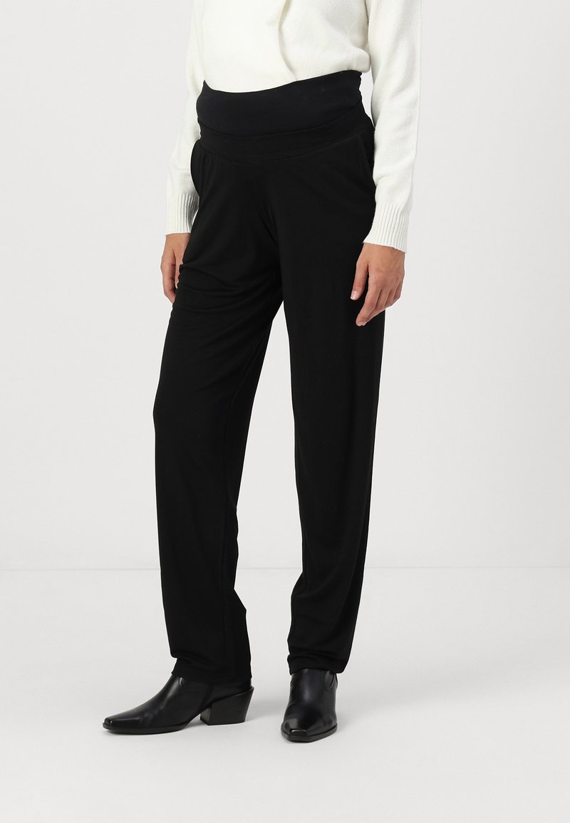 Pantalons noirs avec une taille haute élastique, présentant une coupe ample et une texture lisse. Assortis à de élégants bottillons noirs.