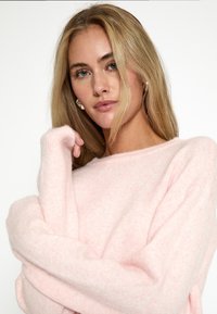 Svetlo ružová, mäkká, oversized mikina s dlhými rukávmi, rebrovanými manžetami a okrúhlym výstrihom, ktorá má voľný strih a jemnú textúru.