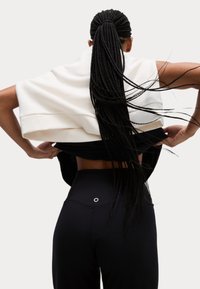 Svarta högmidjade leggings med en cirkulär accent på baksidan. En vit sweatshirt hänger över axlarna och visar hud.