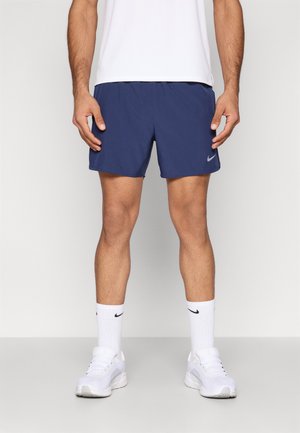 Μπλε σκούρα αθλητικά σορτς με ελαστική μέση, ελαφρύ ύφασμα, πλευρικές τσέπες και λογότυπο Nike. Συνδυασμένα με λευκές κάλτσες και παπούτσια.