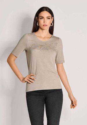 Beige T-shirt met korte mouwen en een ronde halslijn, met uitsparingen en versieringen over de borst. Soepele textuur.