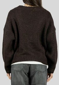 Maglione in maglia marrone scuro con una vestibilità larga e oversize, spalle cadenti e orlo a costine, abbinato a jeans grigi, visto da dietro.