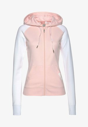 Light pink zip-up hoodie with white sleeves, drawstring hood, and front pockets. Features subtle logo on the side and ribbed cuffs.