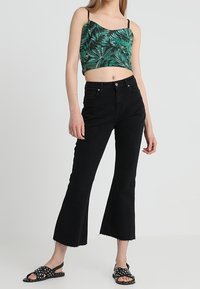 Haut court à motifs de feuilles vertes, jean noir évasé taille haute avec ourlet brut, et sandales noires avec accents à pois.