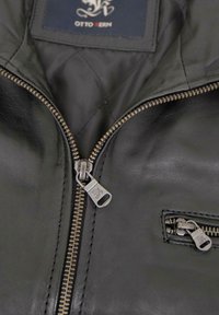 Schwarze Lederjacke innen mit einem gesteppten Futter, ausgestattet mit zwei Reißverschlussverschlüssen und einem Etikett mit der Aufschrift "OTTO KERN." Sichtbare Strukturdetails.