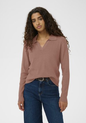 Haut rose clair à manches longues en côtes avec un col en V, associé à un jean bleu foncé, doté d'une ceinture à la taille.
