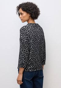 Maglione leopardato in bianco e nero con maniche a tre quarti, texture morbida e scollatura rotonda. Indossato con jeans in denim blu.