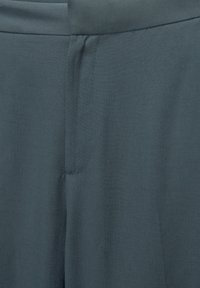 Pantalon ajusté bleu ardoise présentant une texture lisse, un devant plat et des détails de coutures subtiles le long de la ceinture et des poches.