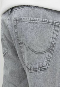 Jeans de mezclilla gris con una superficie texturizada, bolsillos traseros con costuras decorativas y un diseño ajustado.
