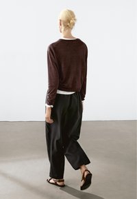 Pull marron, sous-vêtement blanc, pantalon noir à jambes larges et sandales plates. Le design est décontracté, avec un dos bas et des manches roulées.