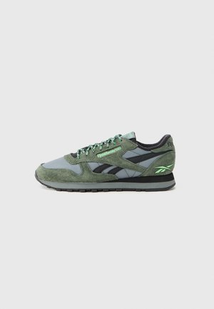 Green and gray sneakers with mesh and suede materials, black accents, and green laces, featuring a textured sole and logo detail.