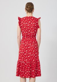 Red floral dress with short ruffled sleeves, fitted bodice, and tiered skirt, featuring a tie at the waist and small white and pink flowers.