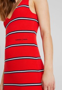 Abito rosso a costine con strisce orizzontali blu navy e bianche e scollatura a V. Logo "Tommy Jeans" mostrato nella zona centrale del design.