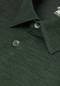 Mörkgrön pikétröja med en texturerad tygkvalitet. Har en klassisk krage och två ljusgröna knappar nära halsringningen.