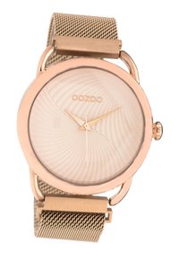 Montre ronde en or rose avec un cadran beige texturé, des aiguilles dorées et un bracelet en maille métallique. Elle dispose d'un fermoir simple pour l'ajustement.