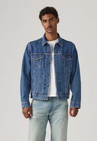 Modrá rifľová bunda s golierom, zapínaním na gombíky vpredu a náprsnými vreckami. Opotrebované svetlomodré rifle. Nosené cez bielu košeľu.