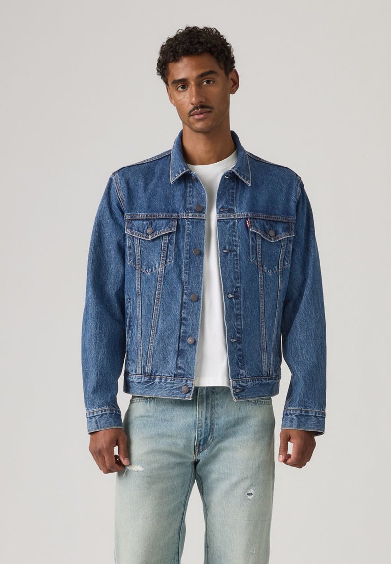 Modrá rifľová bunda s golierom, zapínaním na gombíky vpredu a náprsnými vreckami. Opotrebované svetlomodré rifle. Nosené cez bielu košeľu.